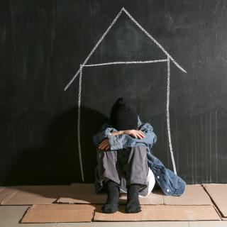 young boy with his head in his arms sitting in front of wall with house drawn on it