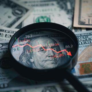 picture of magnifying glass over 100 dollar bill and downward line graph