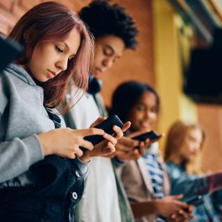 Group of teenagers using mobile phones in hallway at high school